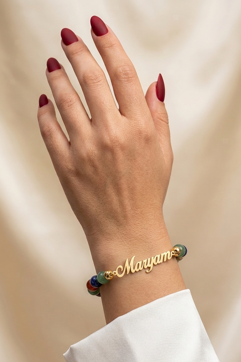 Hand wearing a gold bracelet with 'Maryam' on a beige background