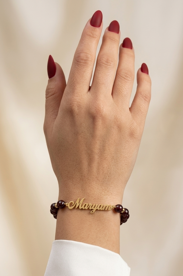 Hand wearing a gold bracelet with brown beads on a beige background