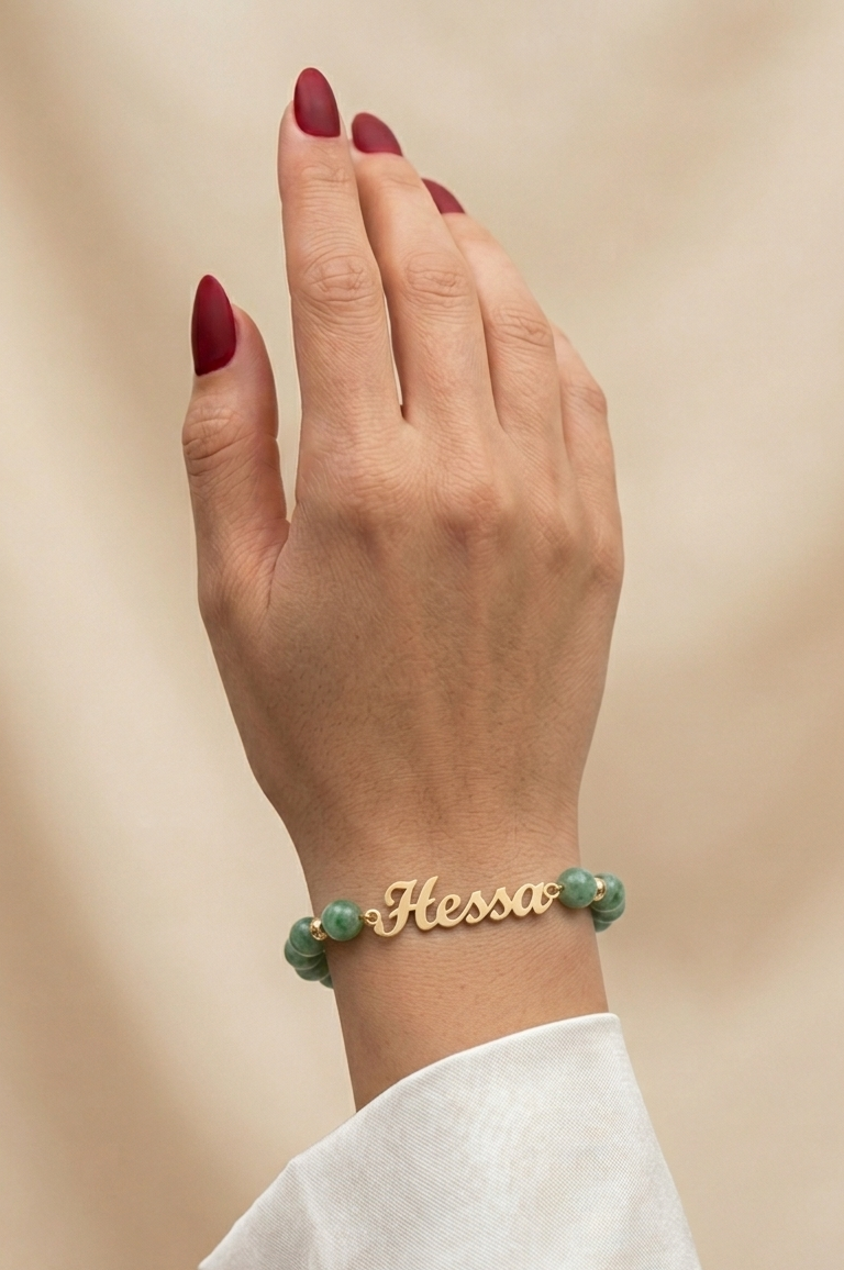 Hand wearing a gold bracelet with green beads on a beige background