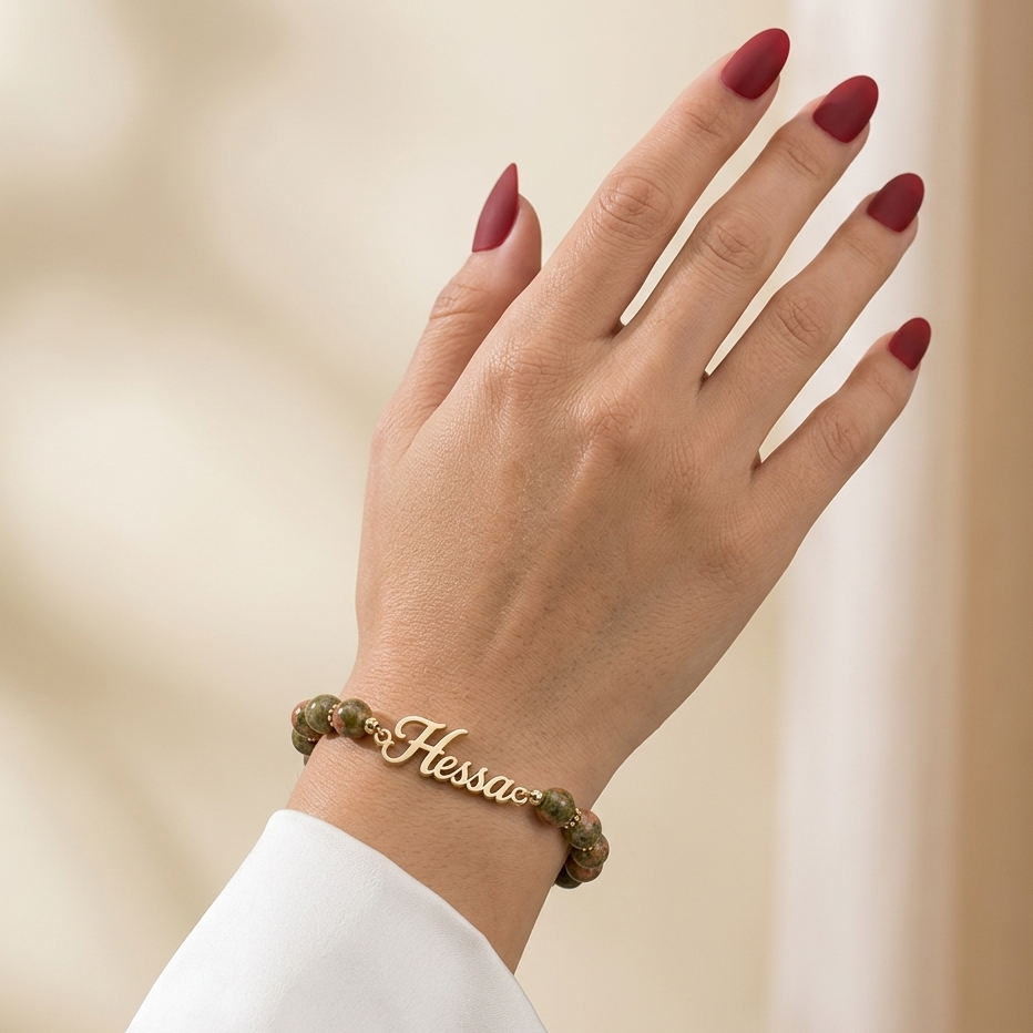 Hand wearing a gold bracelet with 'Hessa' on a beige background