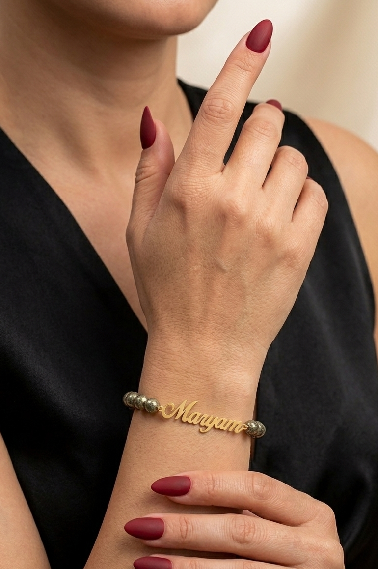 Close-up of a person wearing a gold bracelet with 'Megan' engraved, against a neutral background.
