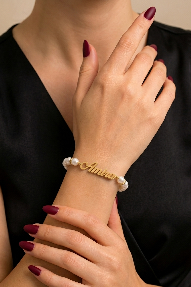 Gold bracelet with pearls on a person's wrist against a black background