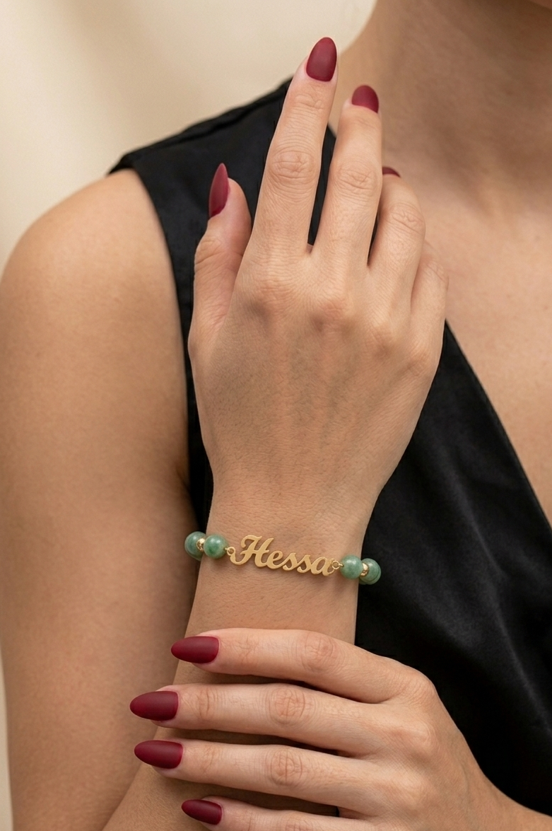 Gold bracelet with green beads on a person's wrist against a neutral background