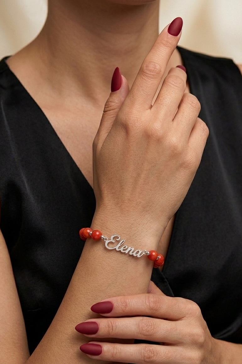 Woman wearing a bracelet with red beads and 'Elena' engraved, against a neutral background.