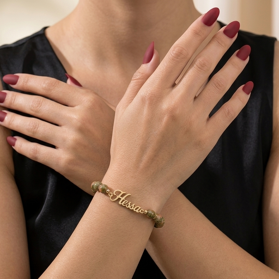 Woman's hands with a gold bracelet featuring the brand 'Hessie' against a neutral background