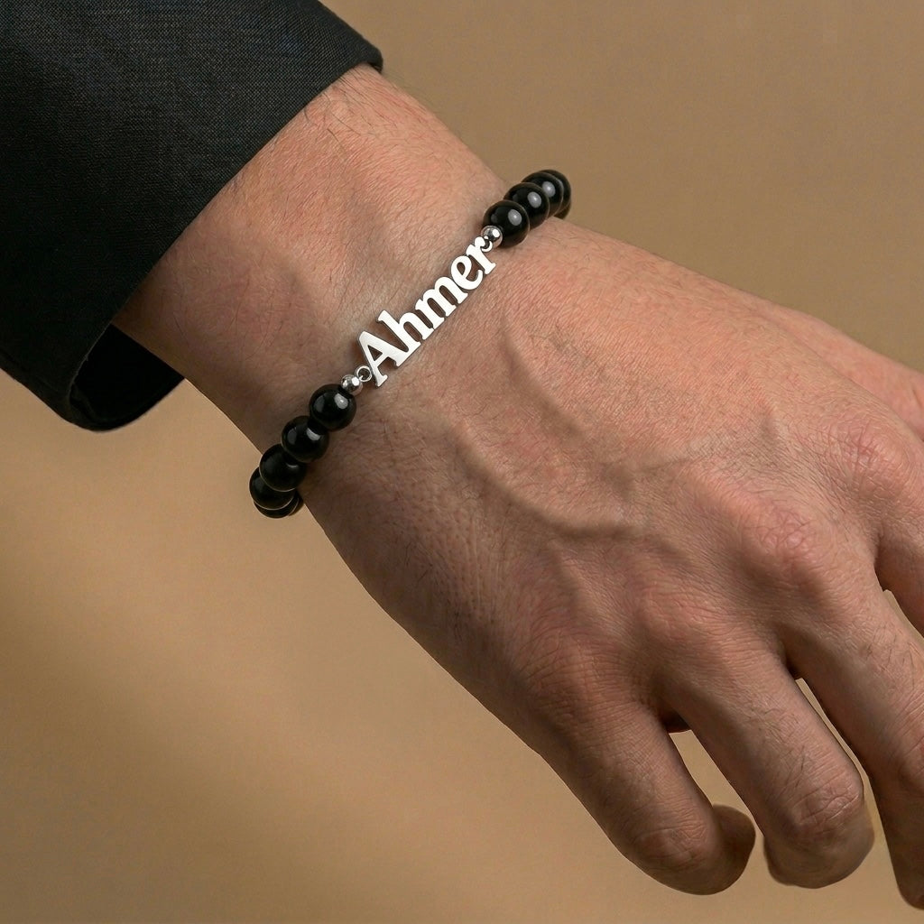Black beaded bracelet with a nameplate on a wrist against a beige background