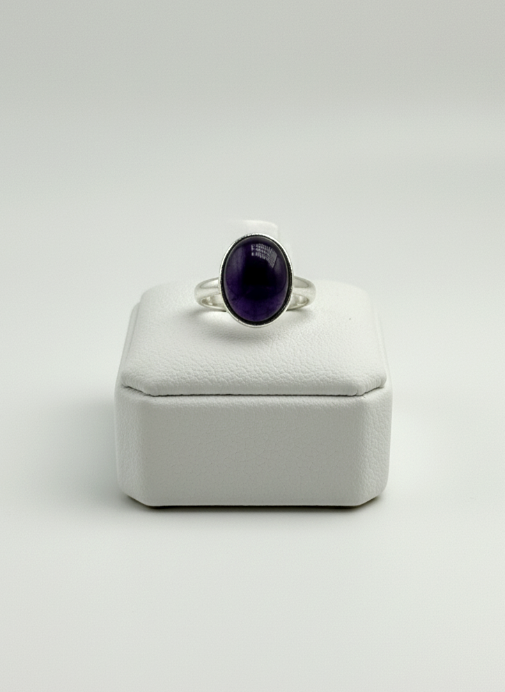 Silver ring with a purple gemstone on a white box against a light gray background