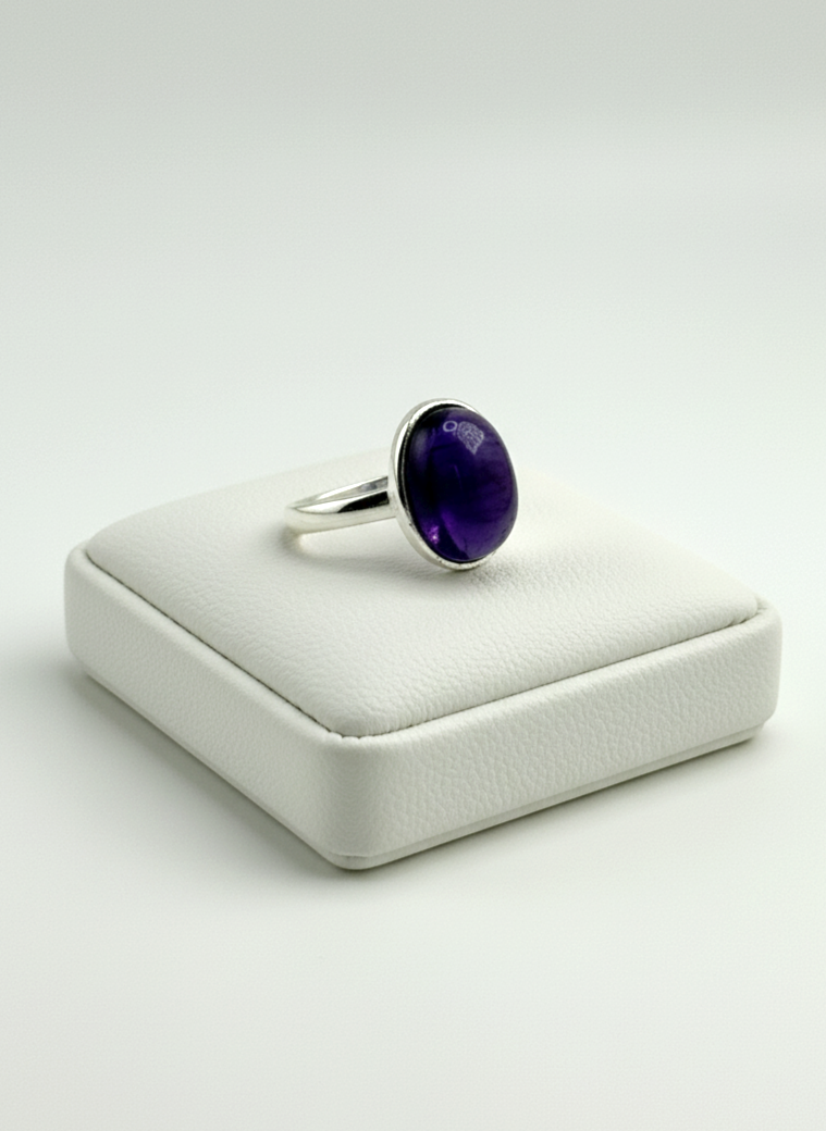 Silver ring with a purple gemstone on a white cushioned stand
