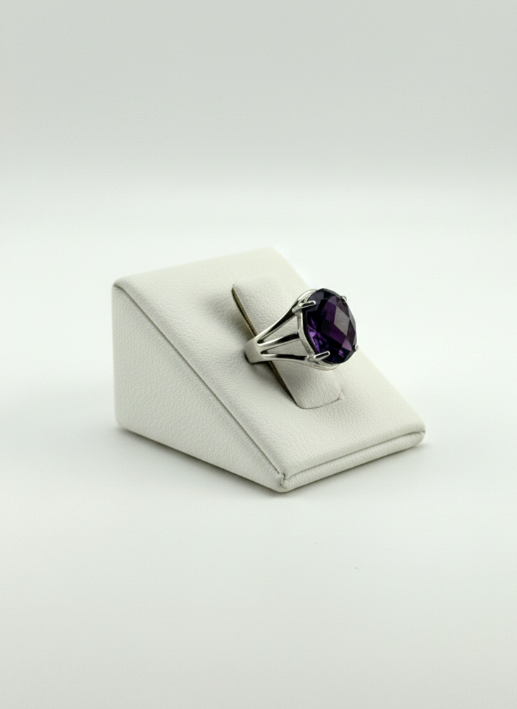 Ring with a purple gemstone on a white wedge display against a light gray background