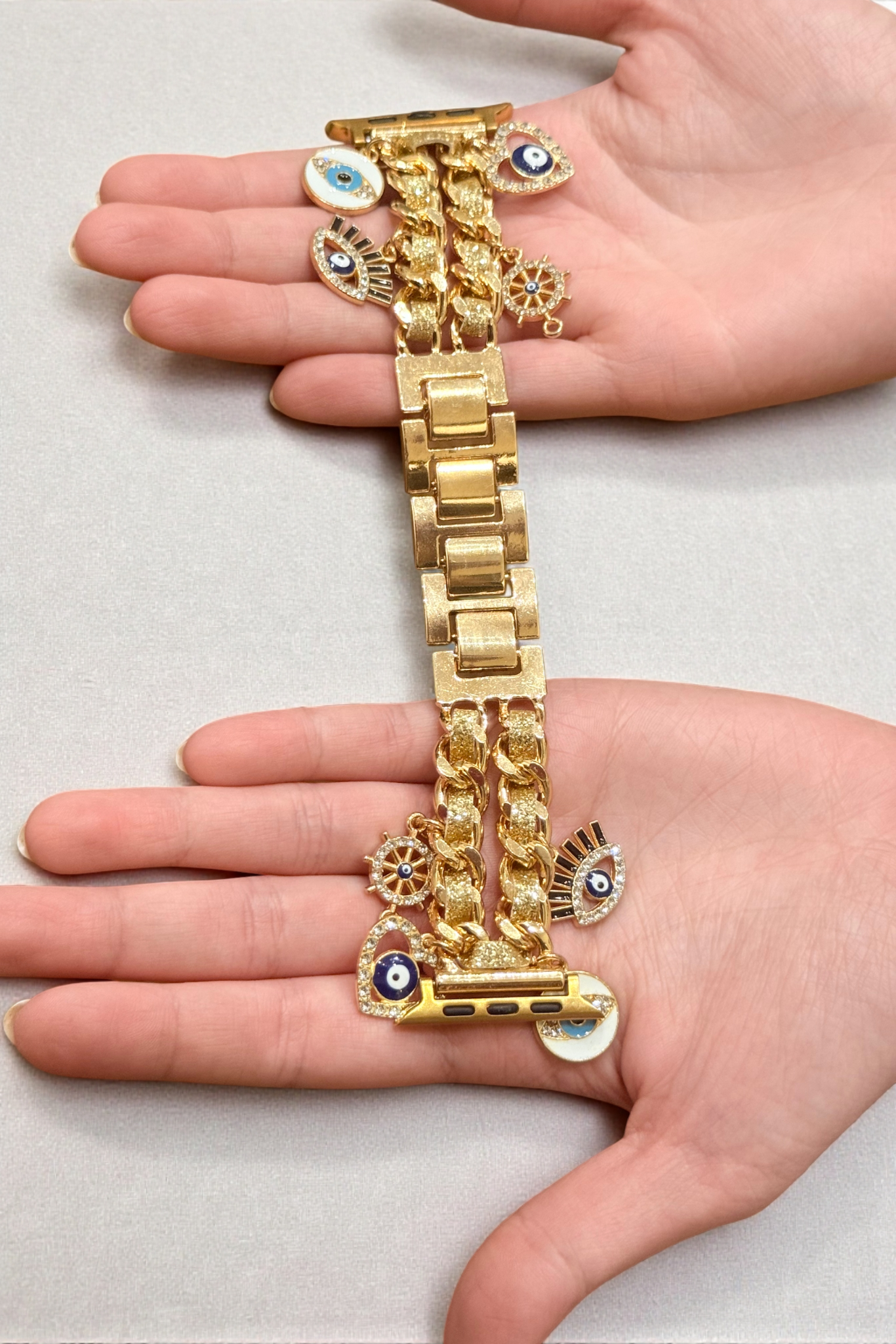 Gold chain and watch on a hand against a light gray background