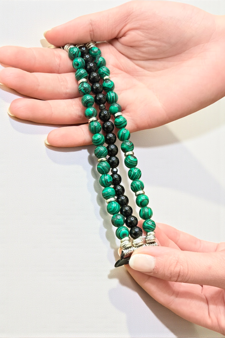 Hand holding a green and black beaded necklace against a white background