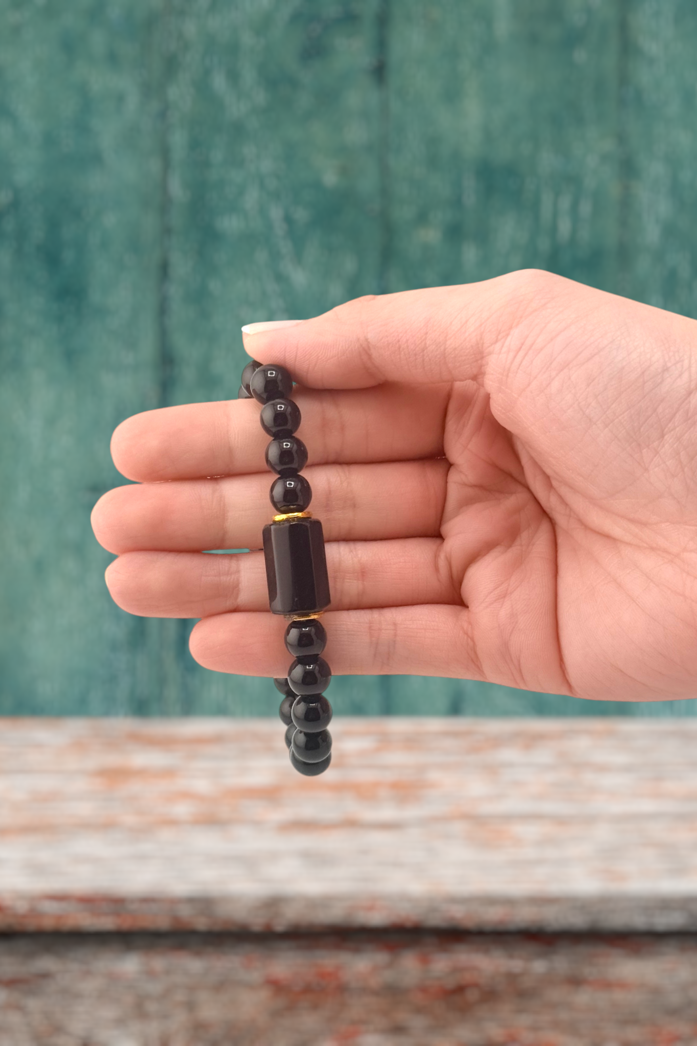 Hand holding a black beaded bracelet against a teal and wooden background
