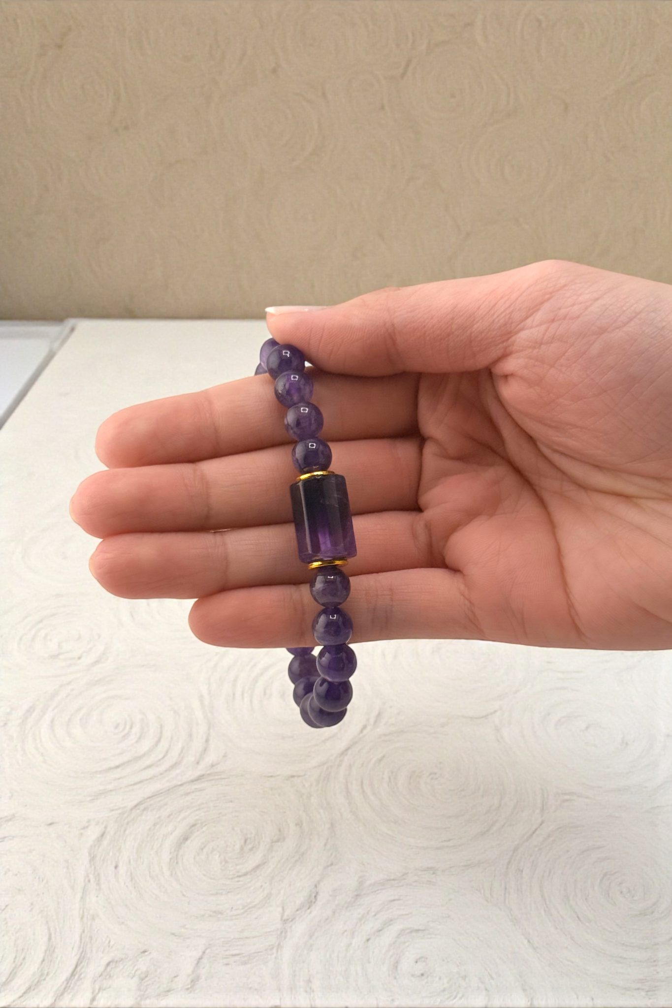 Hand holding a purple beaded bracelet against a neutral background