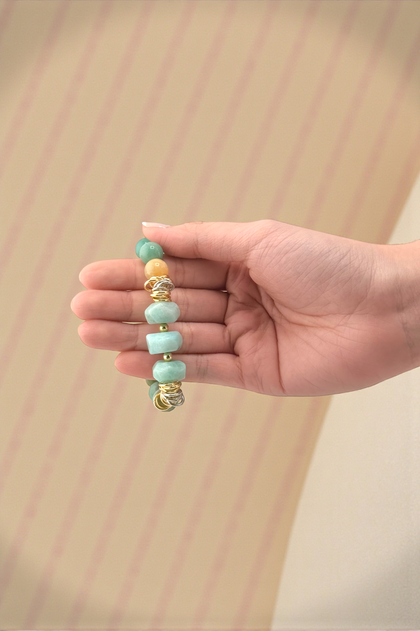 Hand holding a bracelet with turquoise and gold beads against a beige background
