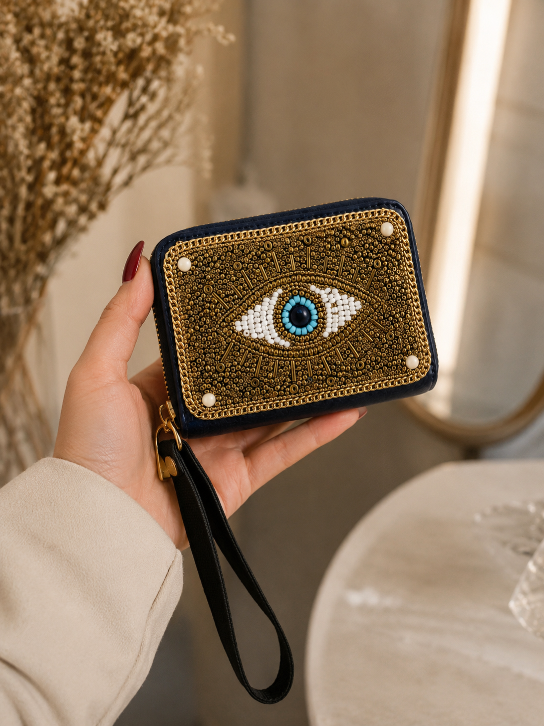 Hand holding a decorative clutch with an eye design against a neutral background