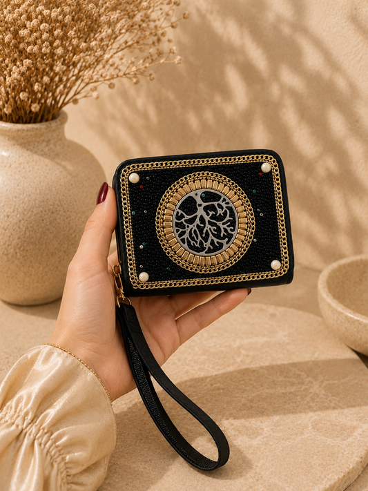 Hand holding a black and gold embroidered clutch with a vase and dried plants in the background