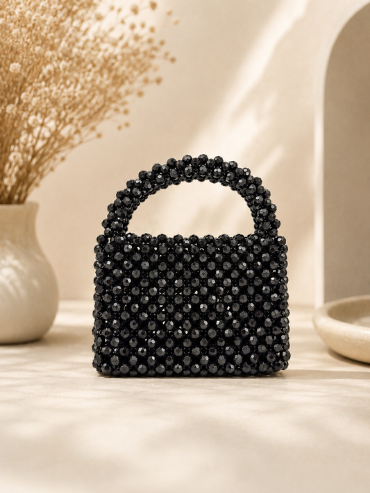 Black beaded handbag on a light surface with decorative elements in the background