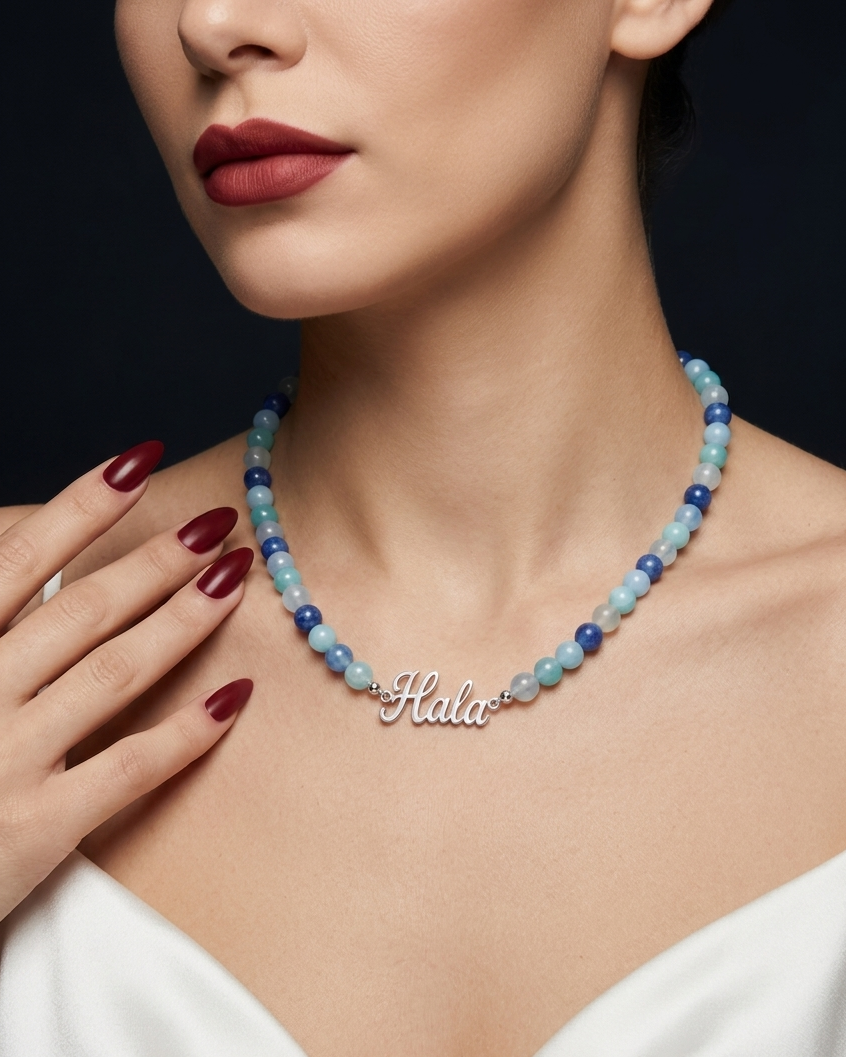 Woman wearing a beaded necklace with a clear 'Hala' pendant against a dark background