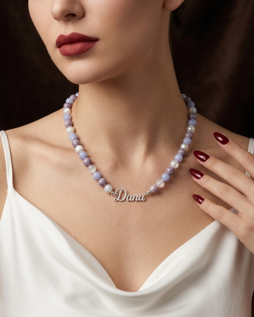 Woman wearing a pearl necklace with a nameplate, set against a dark background.