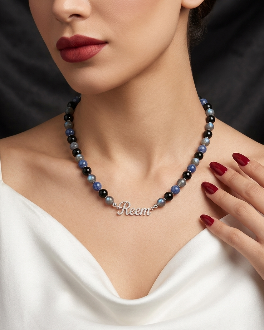Woman wearing a beaded necklace with 'Reem' on it, against a black background.