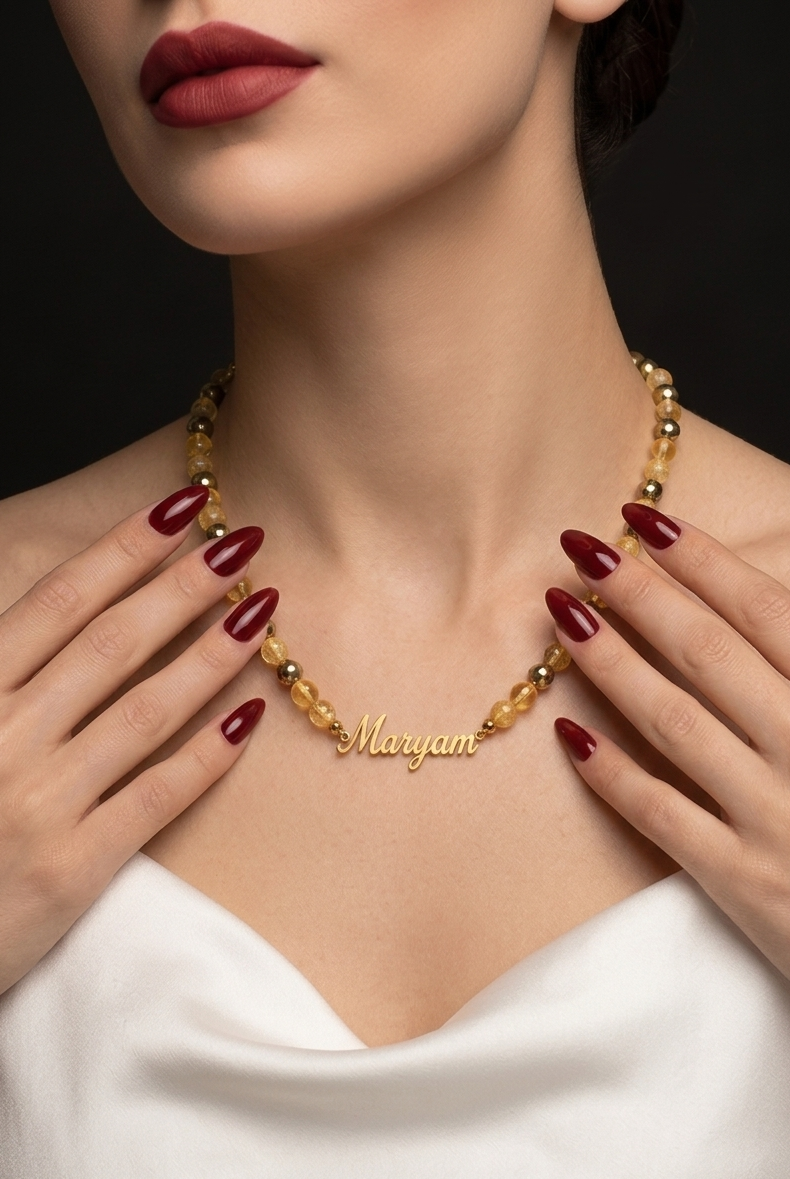 Woman wearing a gold necklace with 'Maryam' engraved, against a dark background