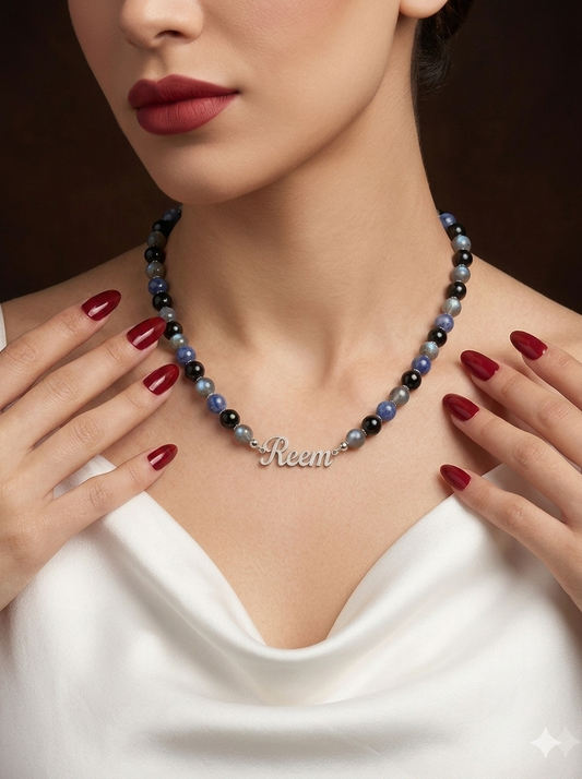 Woman wearing a colorful beaded necklace with 'Reem' engraved, against a dark background.