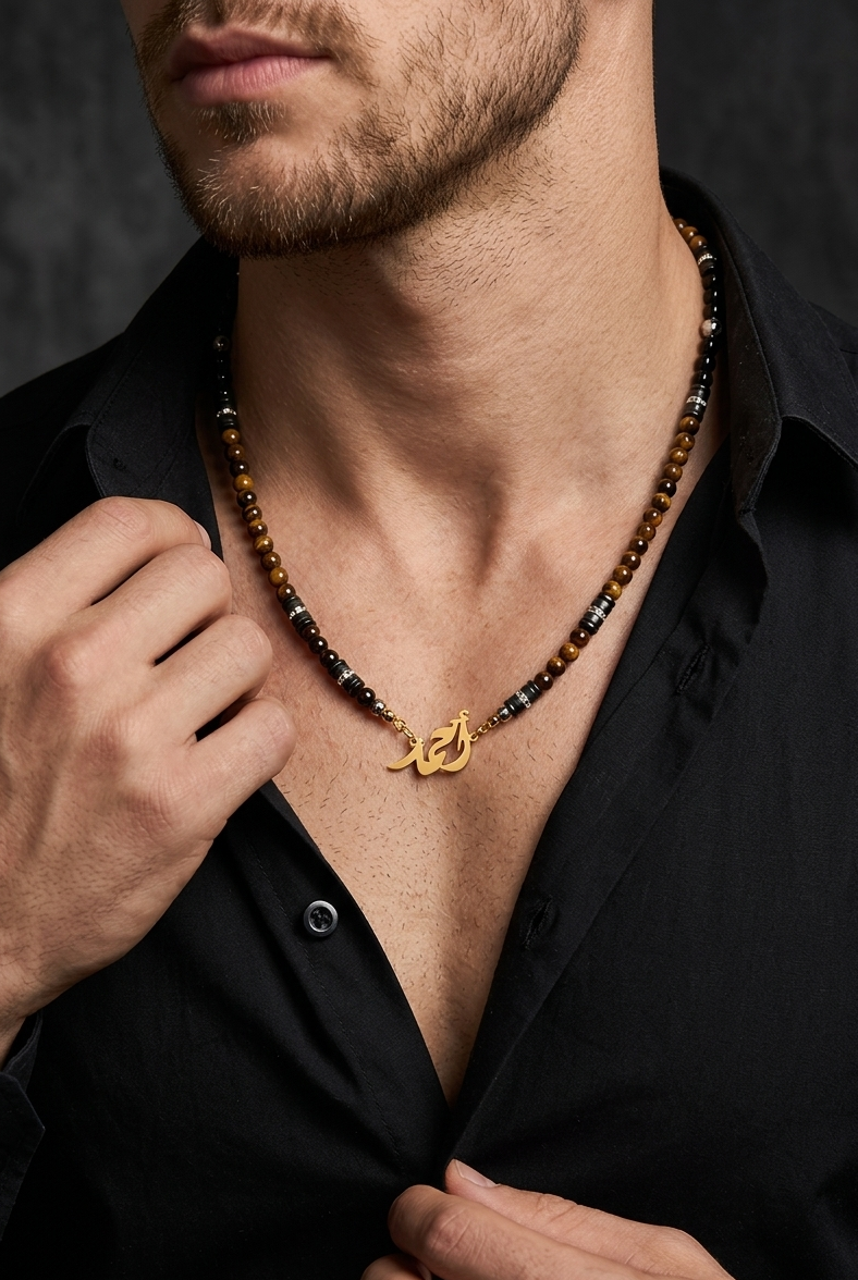 Man wearing a black shirt with a beaded necklace featuring a gold pendant.