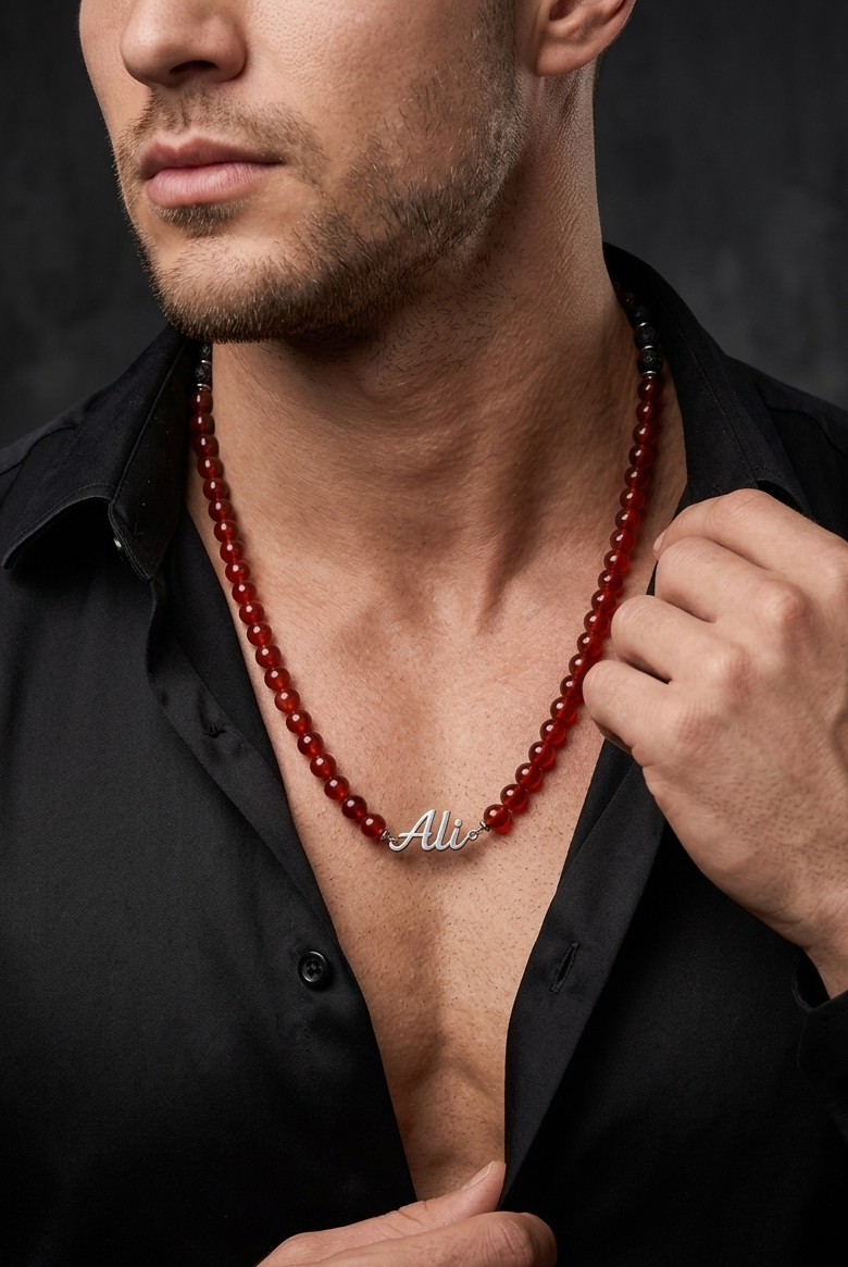 Man wearing a red beaded necklace with a brand logo, against a dark background