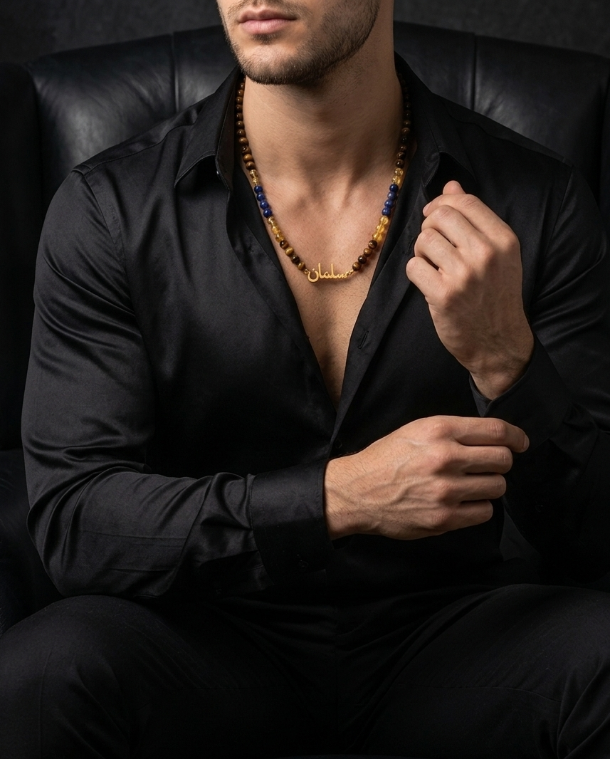 Man wearing a black shirt with a necklace, sitting on a dark leather chair.