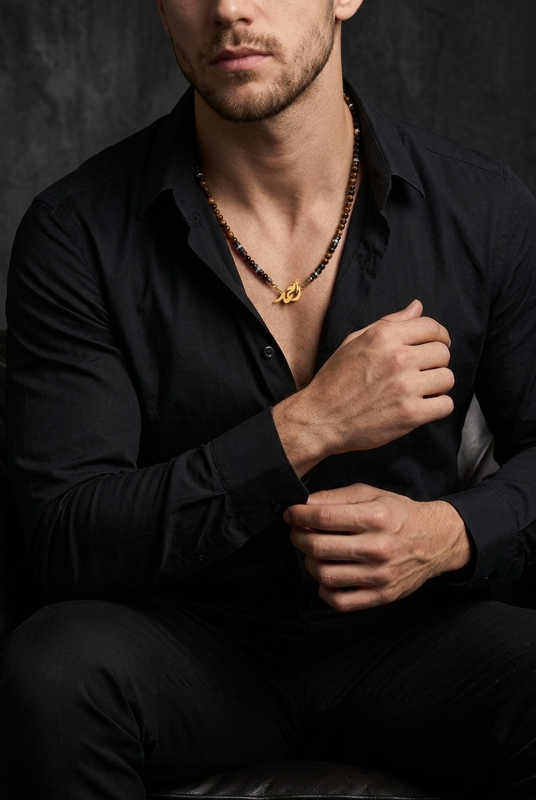 Man wearing a black shirt with a necklace, sitting against a dark background