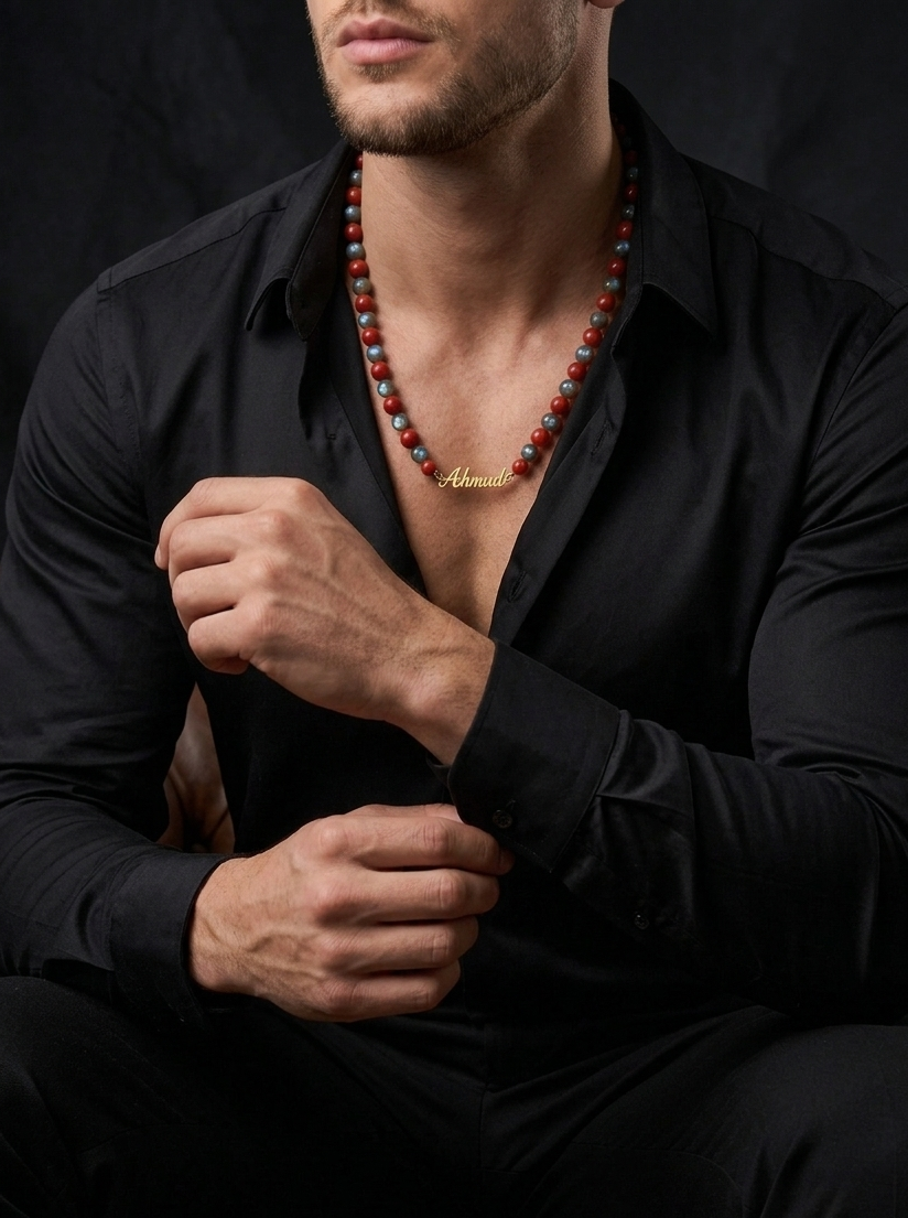 Man wearing a black shirt and a necklace with a brand name, sitting against a dark background.