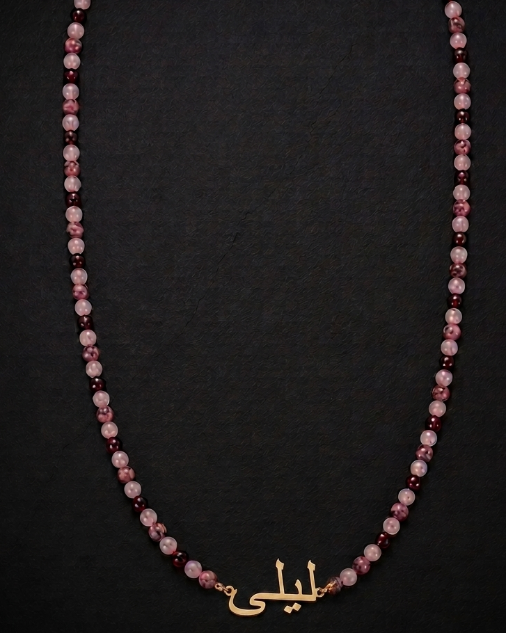 Necklace with pink and red beads and a gold nameplate on a black background