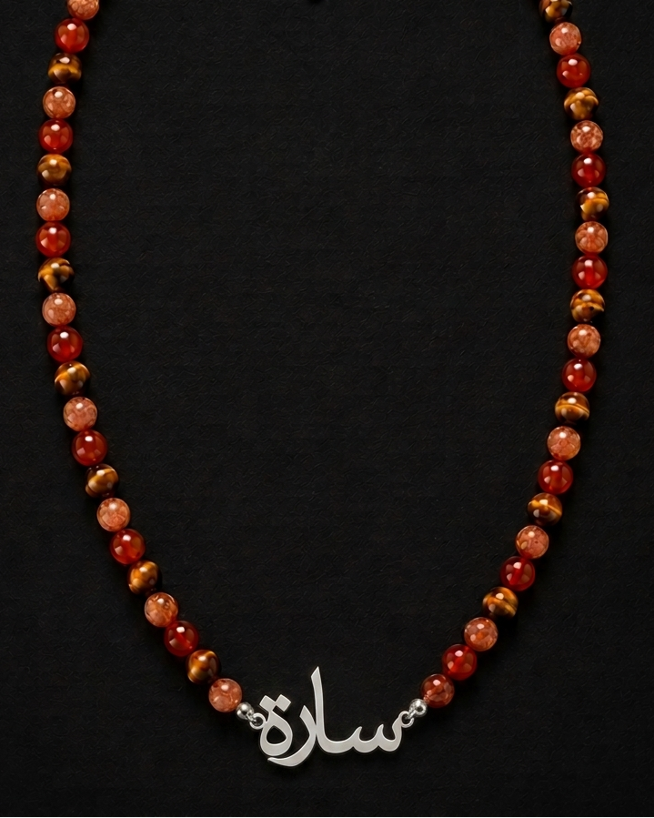 Necklace with red and gold beads and a silver nameplate on a black background