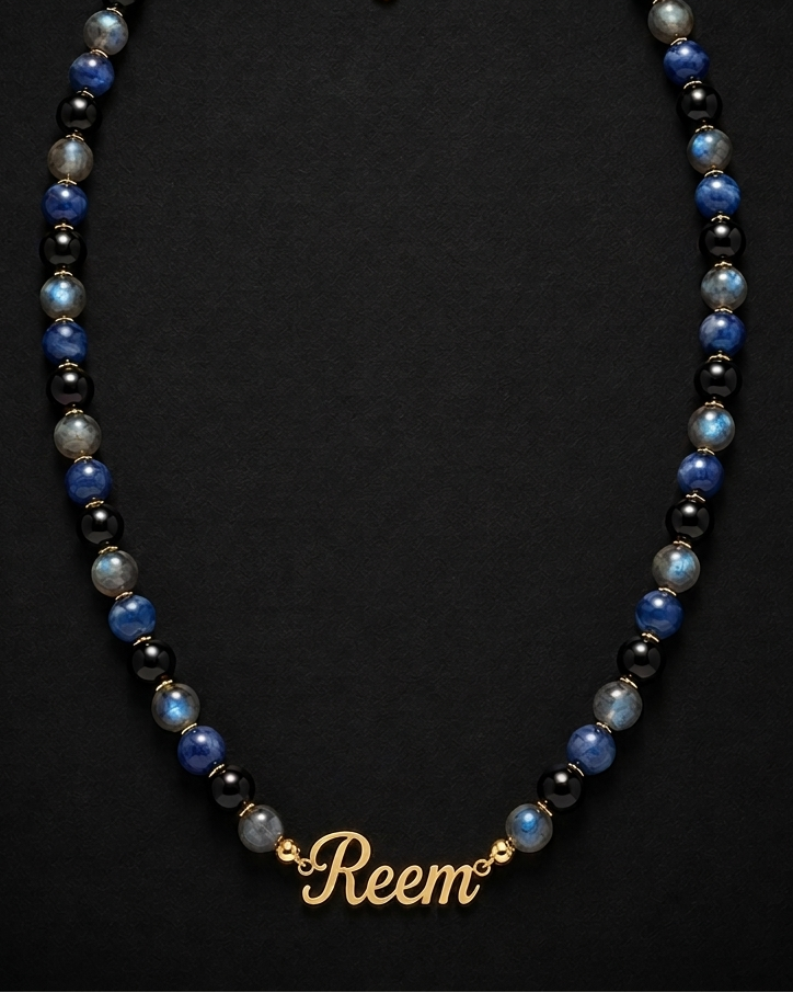 Necklace with blue and black beads and a gold 'Reem' charm on a dark background