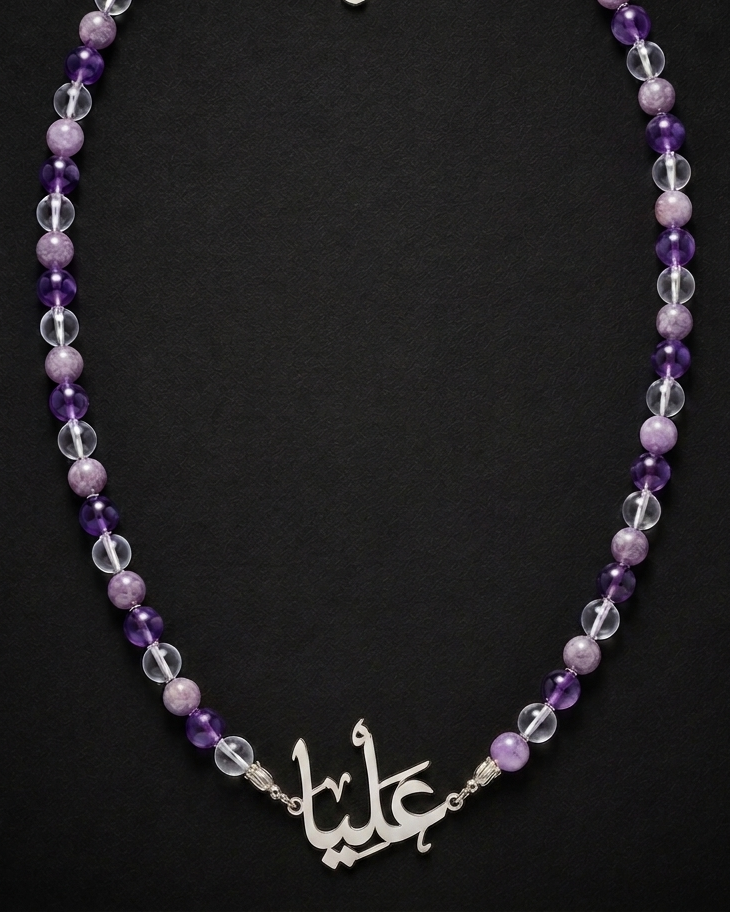 Necklace with purple and clear beads and a silver 'love' charm on a black background