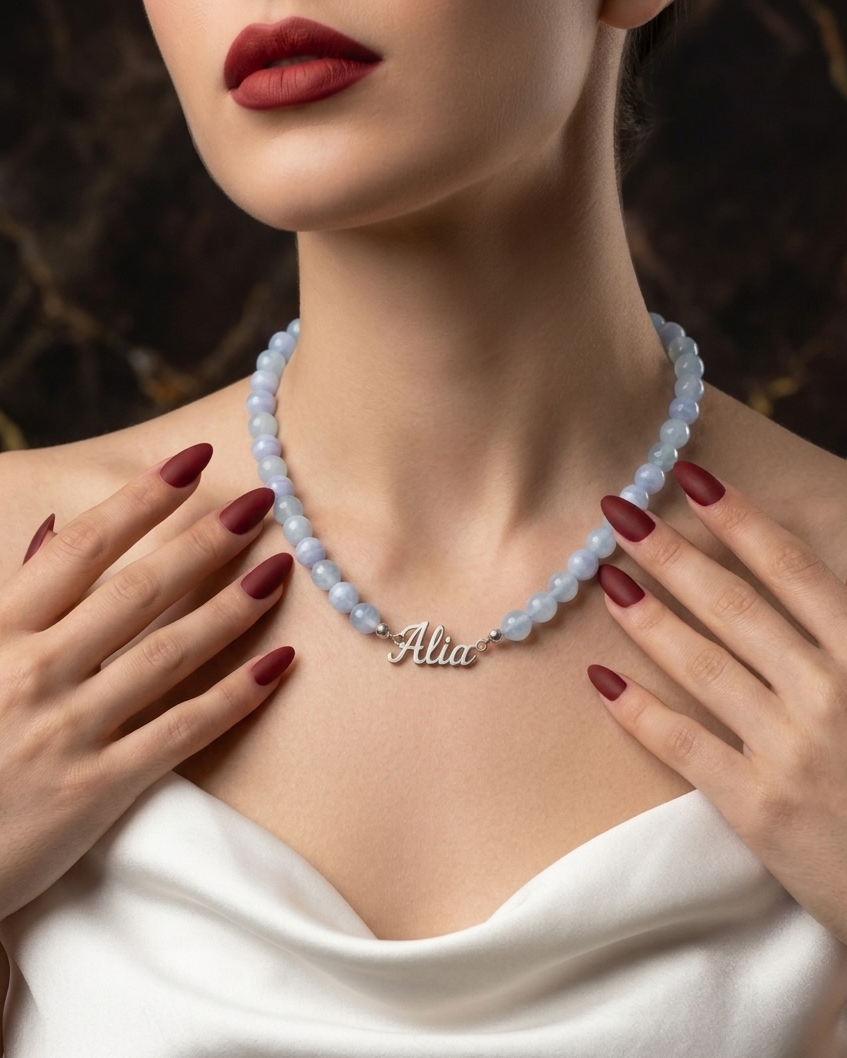 Woman wearing a necklace with a 'Alia' pendant, hands gently touching the neckline.