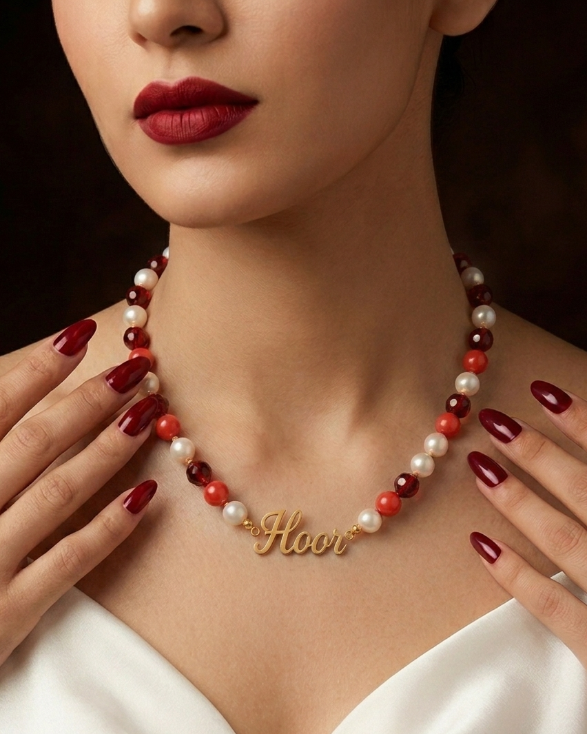 Woman wearing a red and white pearl necklace with a gold 'Flower' pendant, against a dark background.