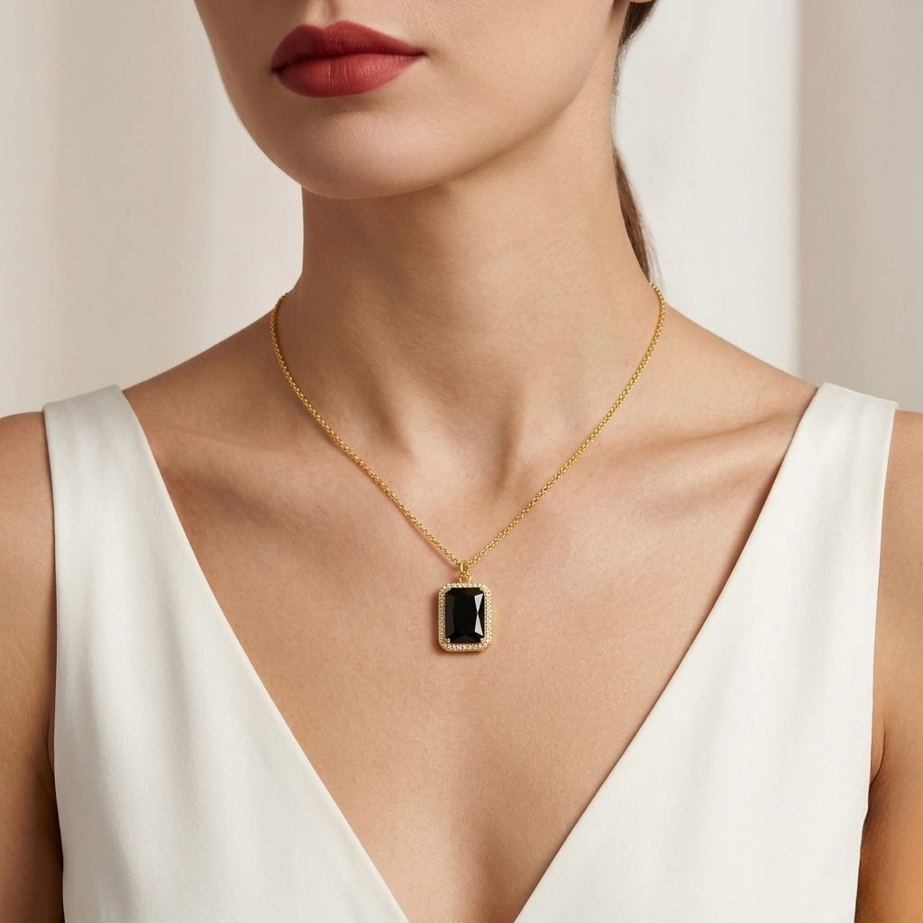 Gold necklace with a black pendant worn by a model against a neutral background