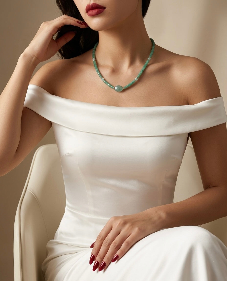 Woman wearing a white off-shoulder dress and a green necklace against a neutral background