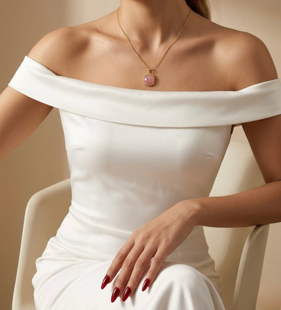Woman wearing a white off-shoulder dress with a gold necklace featuring a pink gemstone.