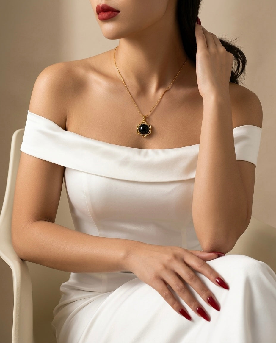 Woman wearing a white off-shoulder dress with a gold necklace featuring a black pendant.