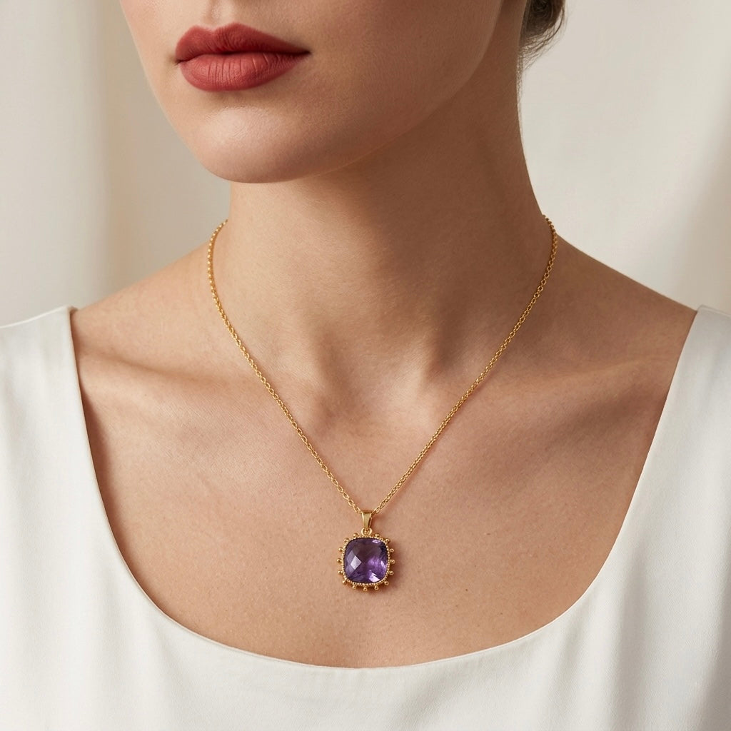Gold necklace with a purple pendant worn by a person against a neutral background
