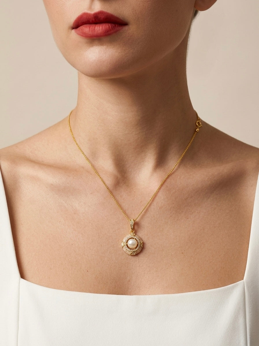 Gold necklace with a pearl pendant worn by a person against a neutral background
