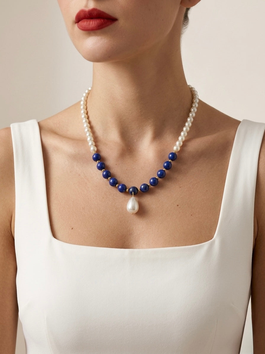 Pearl and blue bead necklace worn by a person in a white top against a neutral background