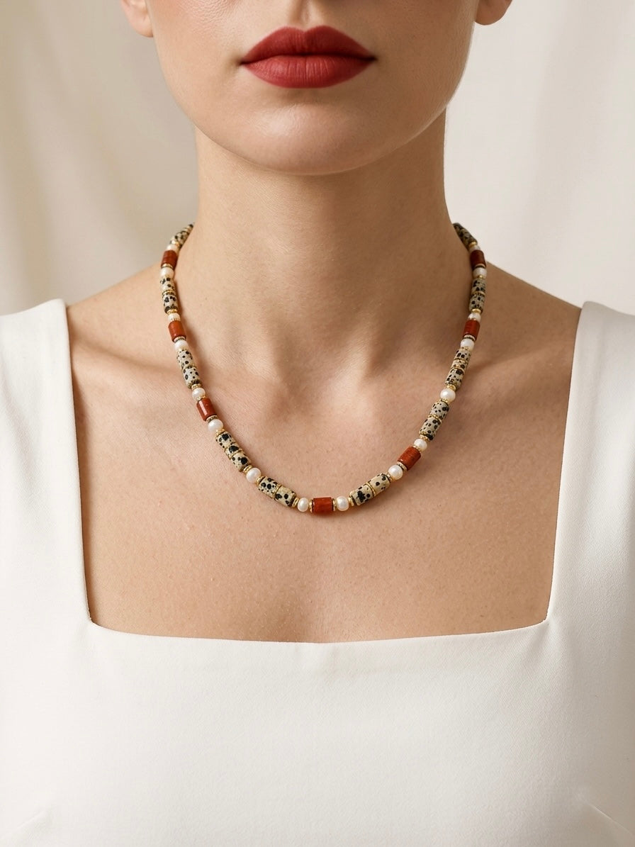 Necklace with red and white beads worn by a person against a neutral background
