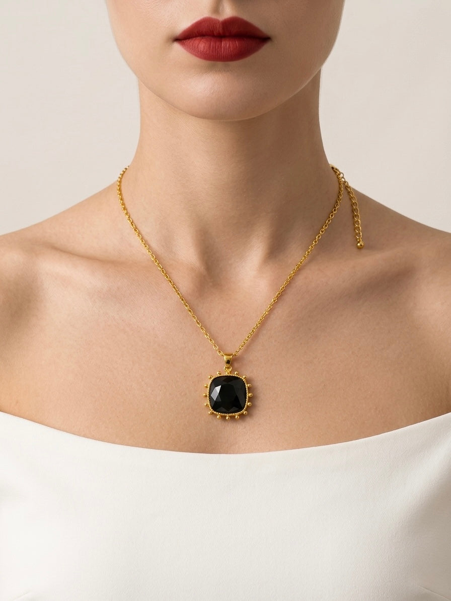 Gold necklace with a black pendant worn by a model on a neutral background