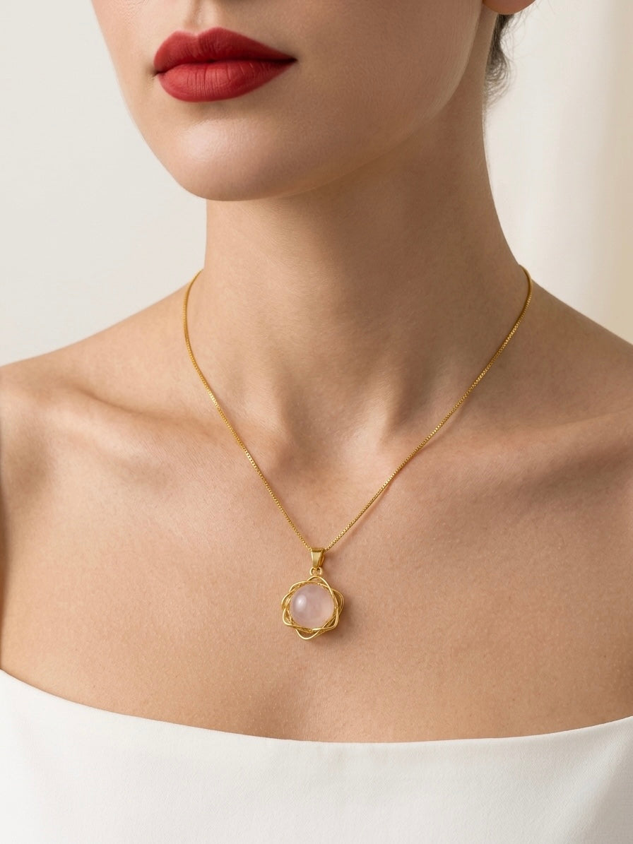 Gold necklace with a pink pendant worn by a model on a plain background