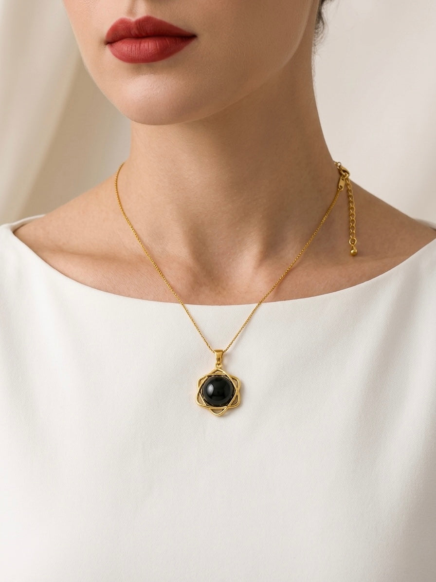 Gold necklace with a black pendant worn by a person against a neutral background