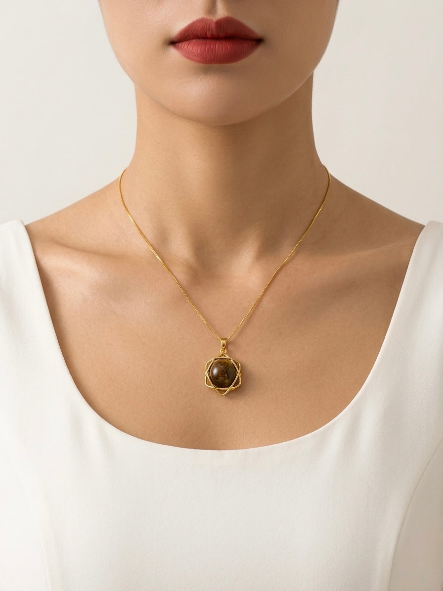 Gold necklace with a pendant worn by a person in a white top on a light background
