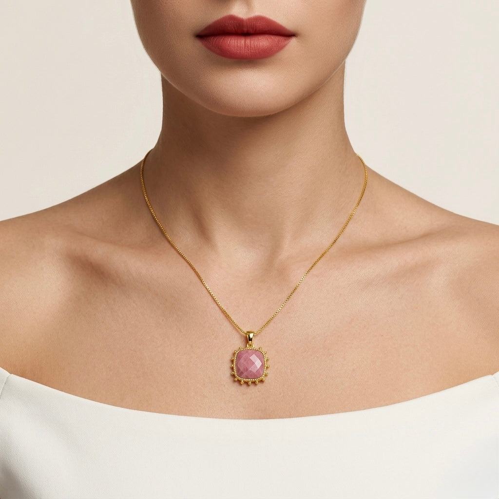 Gold necklace with a pink pendant worn by a model on a neutral background